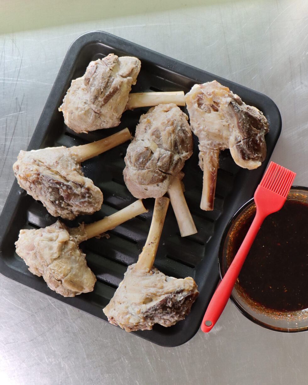 A tray of braised lamb shanks, perfectly cooked and ready for the next step. A basting brush awaits, ready to baste with delicious BBQ sauce!