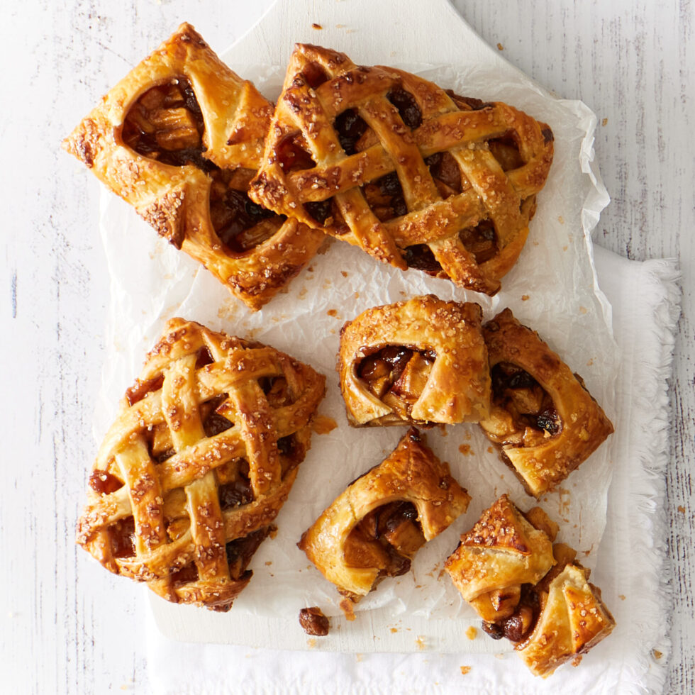 Golden apple hand pies with verjuice-soaked sultanas with lattice tops on a white board and background.