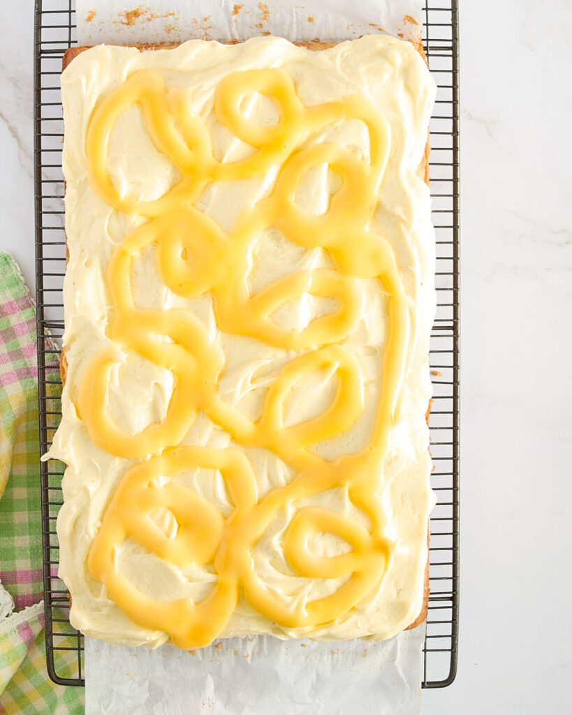 The frosted cake has been piped with lemon curd on its cooling rake.