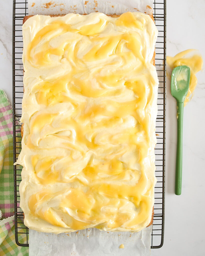 The lemon curd has been swirled through the frosting and the spatula used rests on the marble bench.