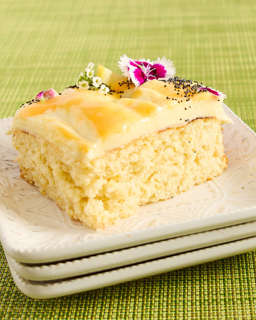 A slice of lemon curd swirl cake on a stack of square white ceramic plates.