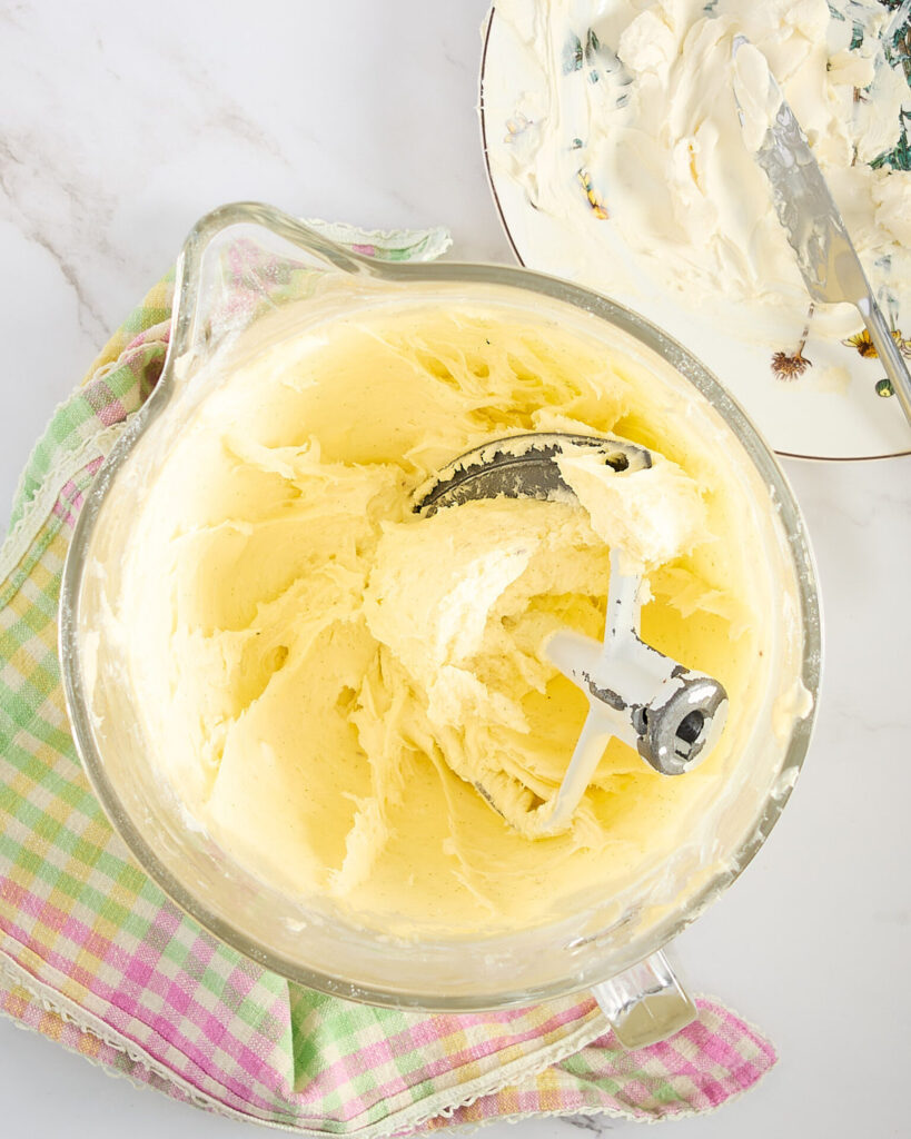 Smooth vanilla cream cheese frosting in the mixer resting on a pastel plaid tea towel.