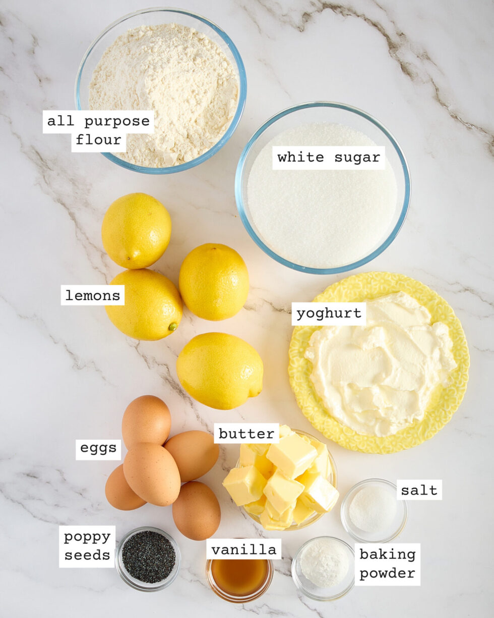 Labelled lemon poppy seed cake ingredients set out on a white marble bench top.
