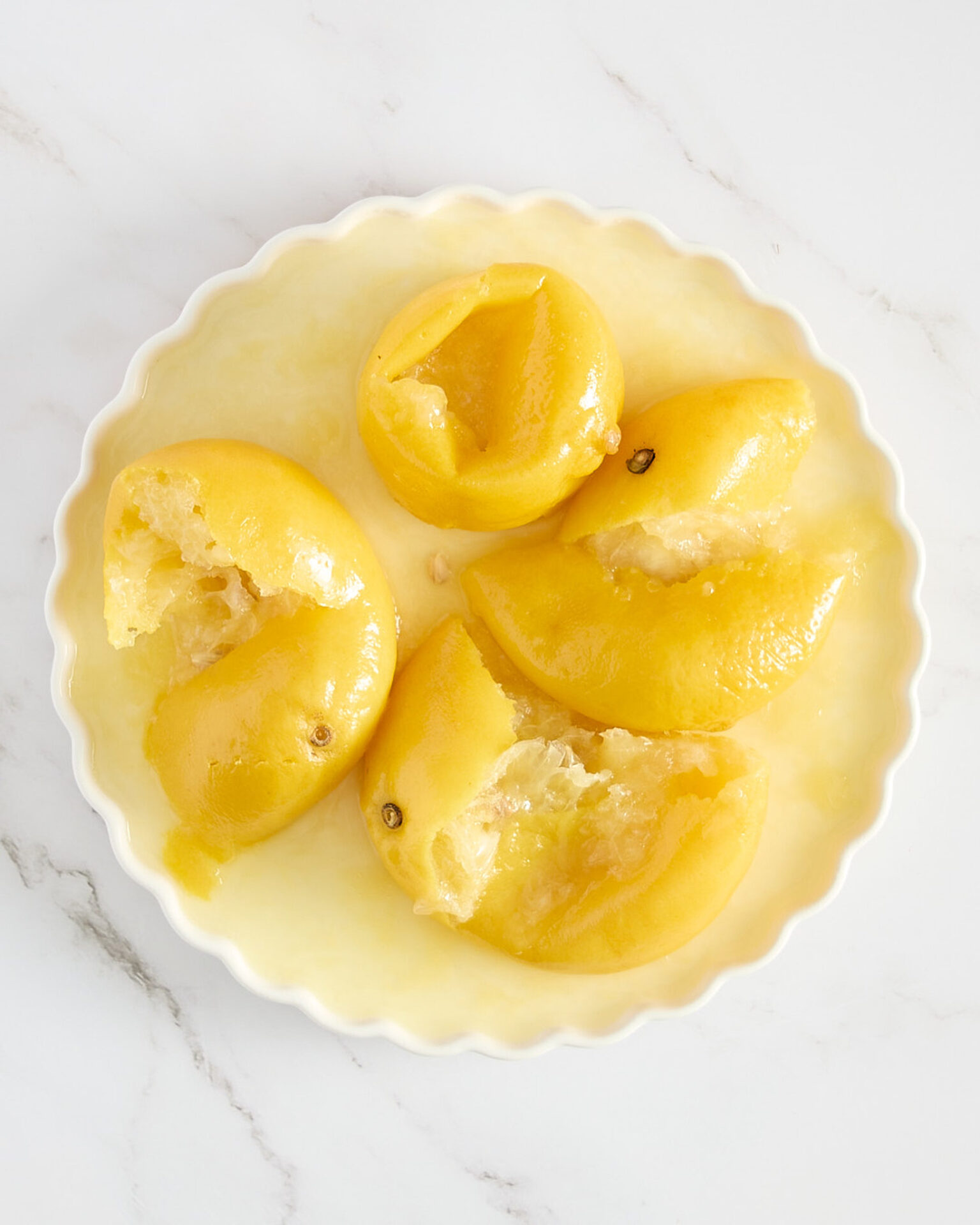 Cooked lemons with seeds removed in a white ceramic dish on a marble bench.