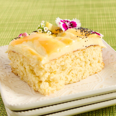 A slice of lemon curd swirl cake on a stack of square white ceramic plates.