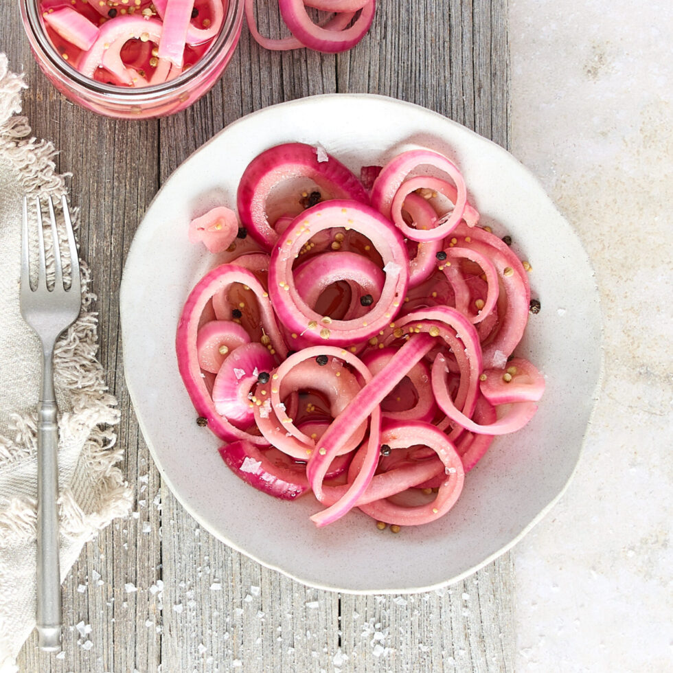 A dish of pickled red onion accompanied by a jar of pickles completes the place setting.