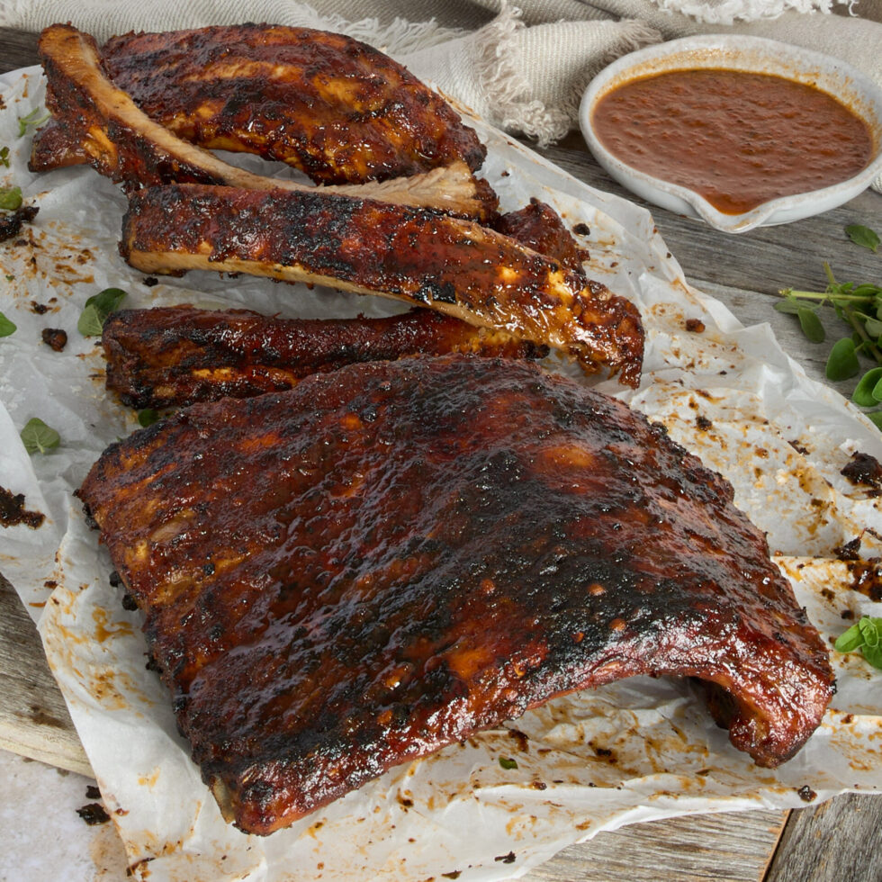 Sticky, succulent smoky chipotle BBQ ribs served on a wooden board with a side dish of sauce.