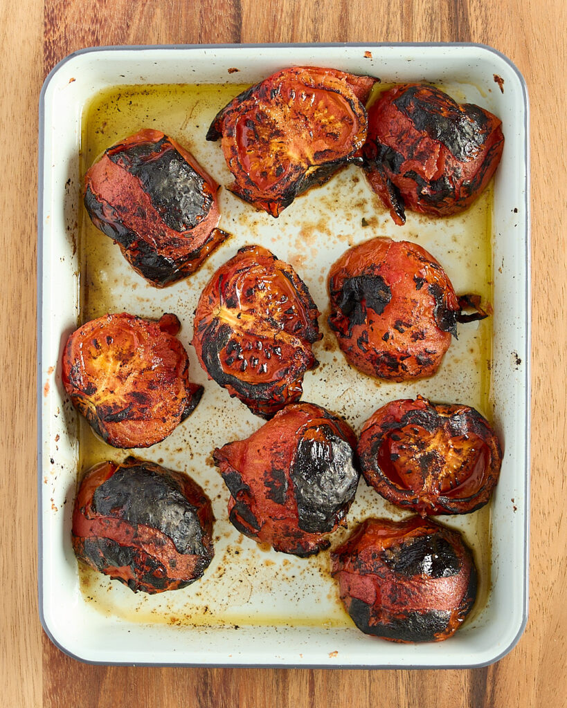 Charred roasted tomatoes in a white ceramic roasting pan.