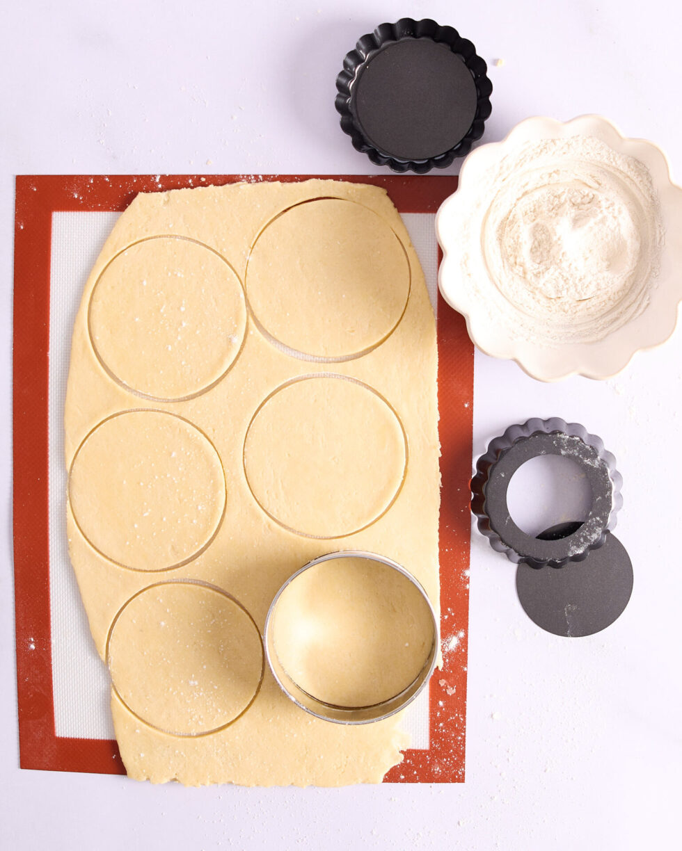 Rolled out pastry with six circles cut and ready for the tart tins.