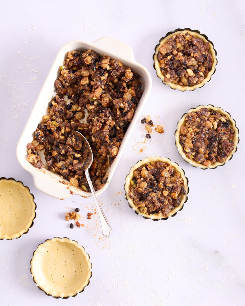 Three of five pastry-lined tart tins filled and a rectangular white ceramic dish of homemade fruit mince.