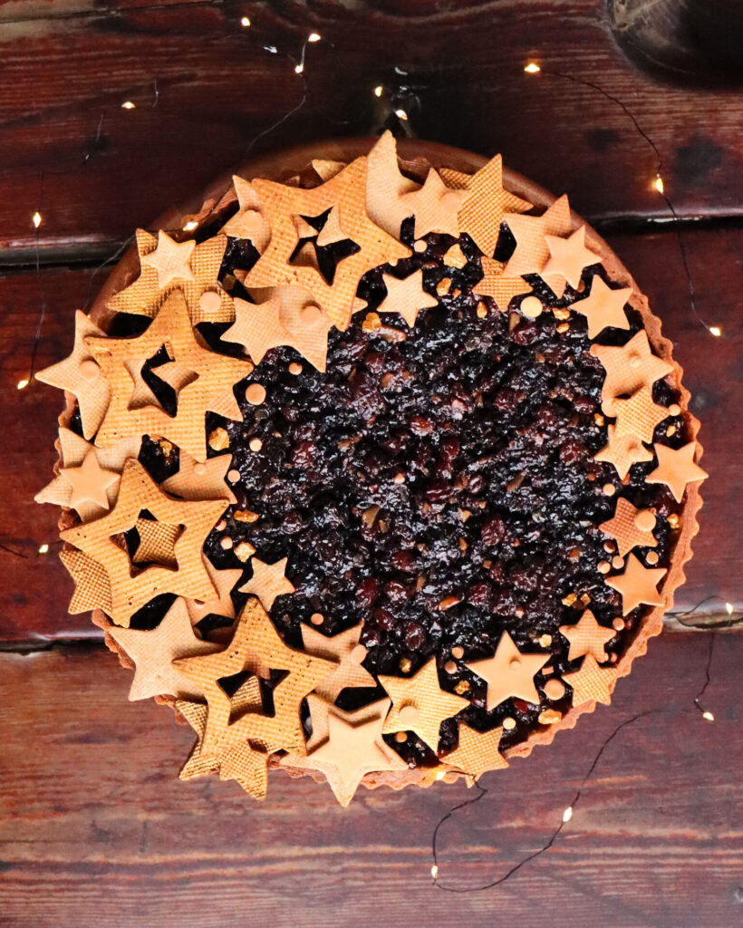 Holiday season fruit mince pie decorated with golden pie crust stars on a dark coloured wooden table top.
