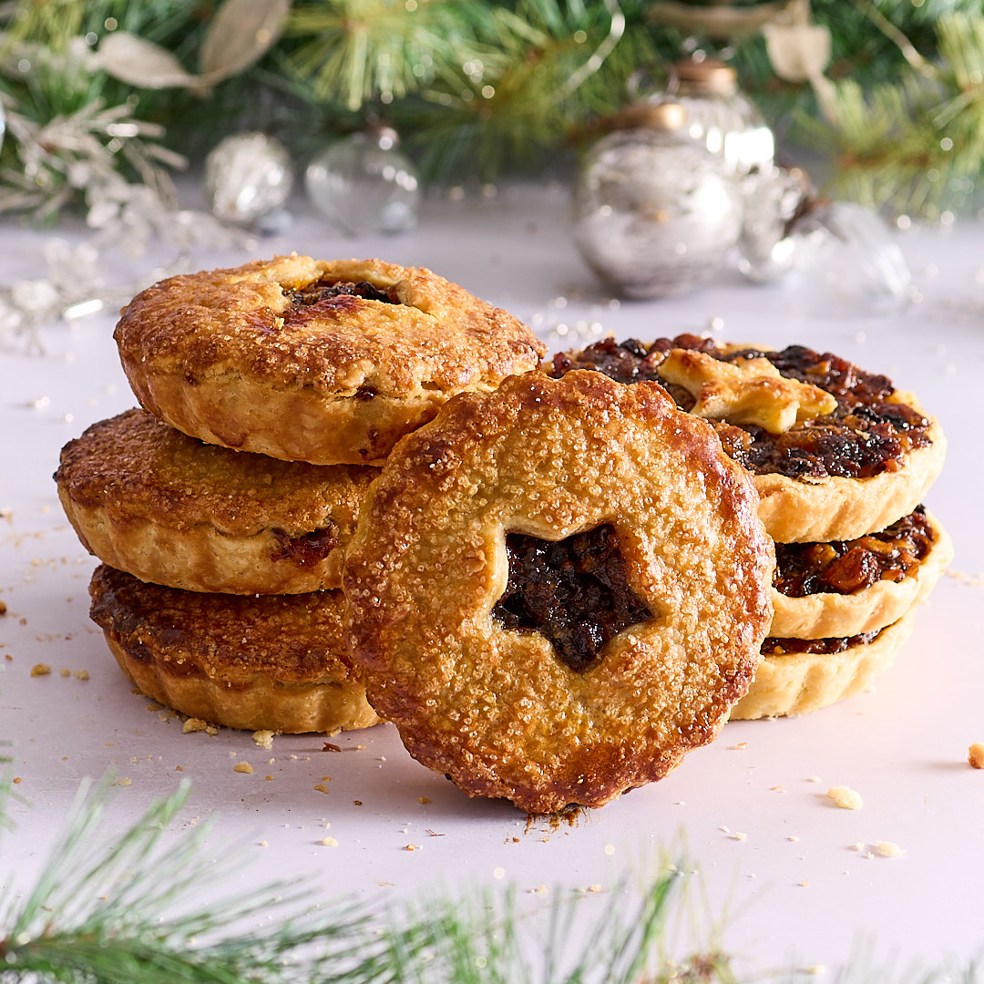 Seven golden brown fruit mince tarts surrounded by festive decorations.