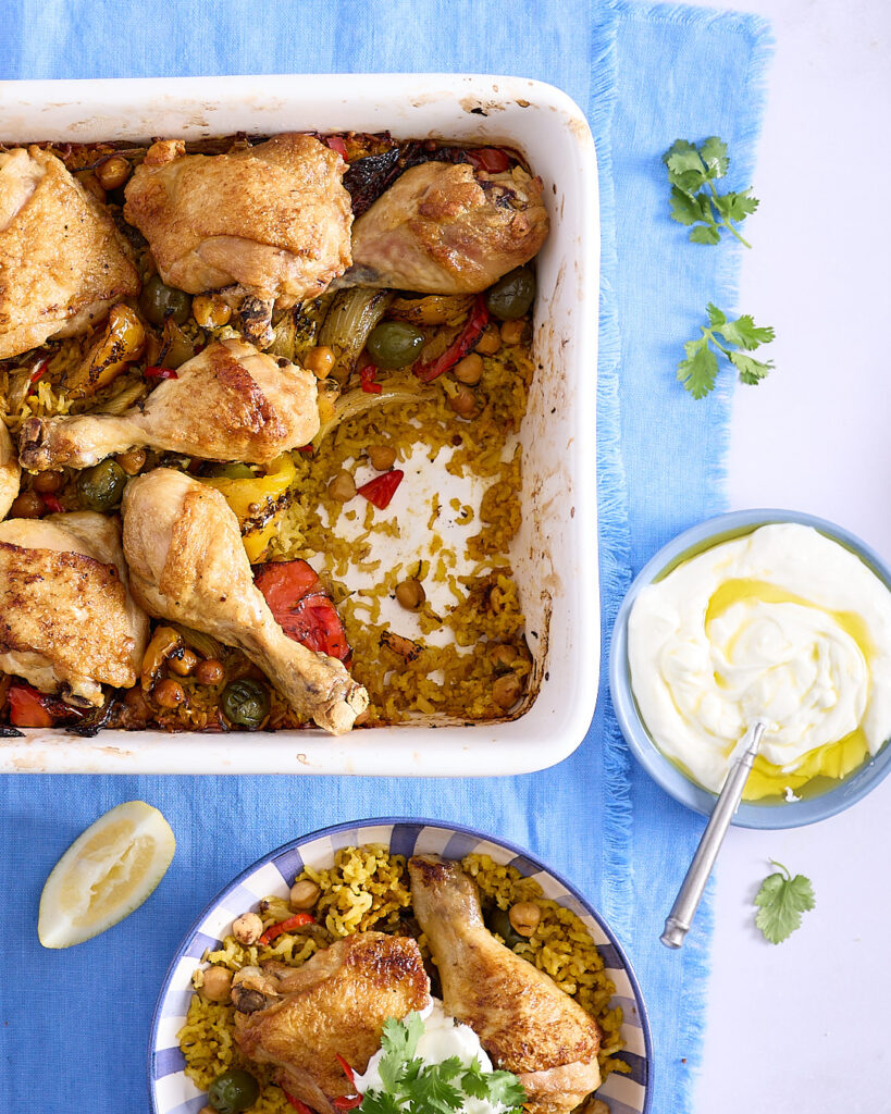 One pan Moroccan chicken and rice in a white ceramic baking dish and a served dish ready to eat on a blue linen napkin.