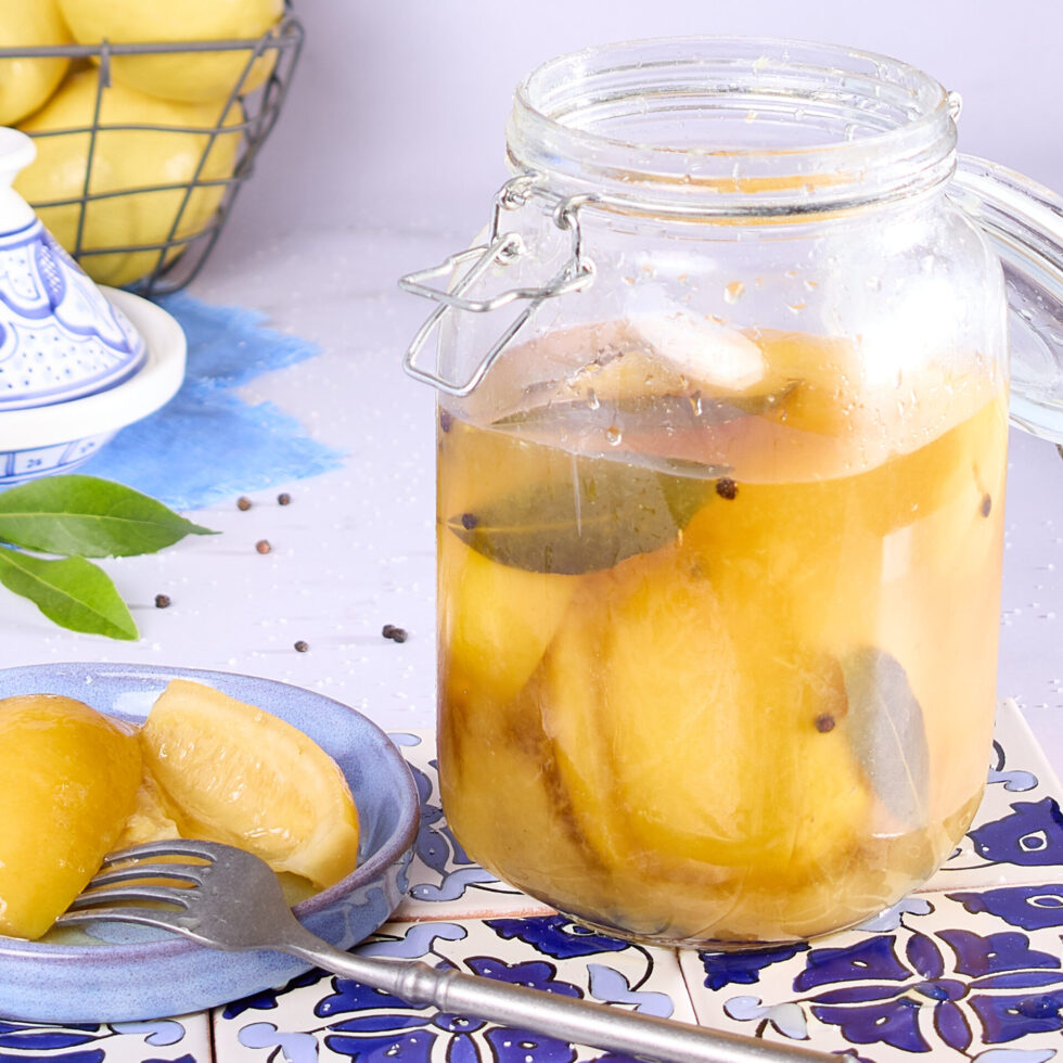 Jar of lacto-fermented lemons ready to be used sitting on Moroccan blue tiles.