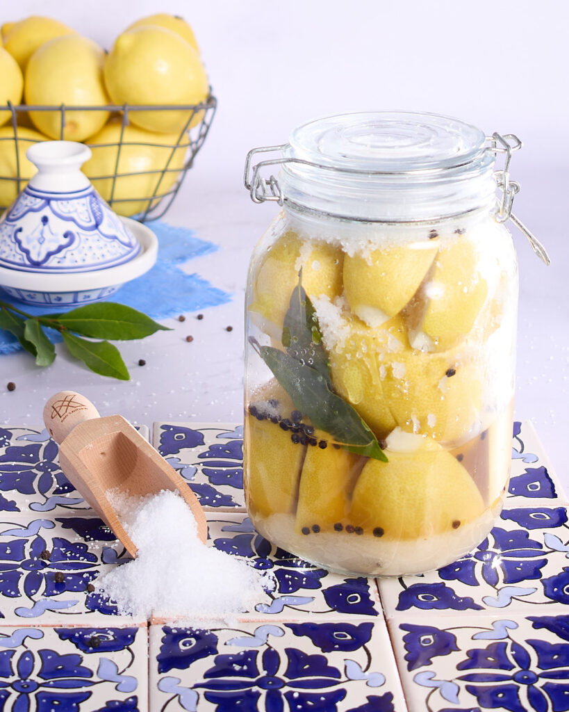 Packed jar of salted lemons sitting on Moroccan blue tiles.