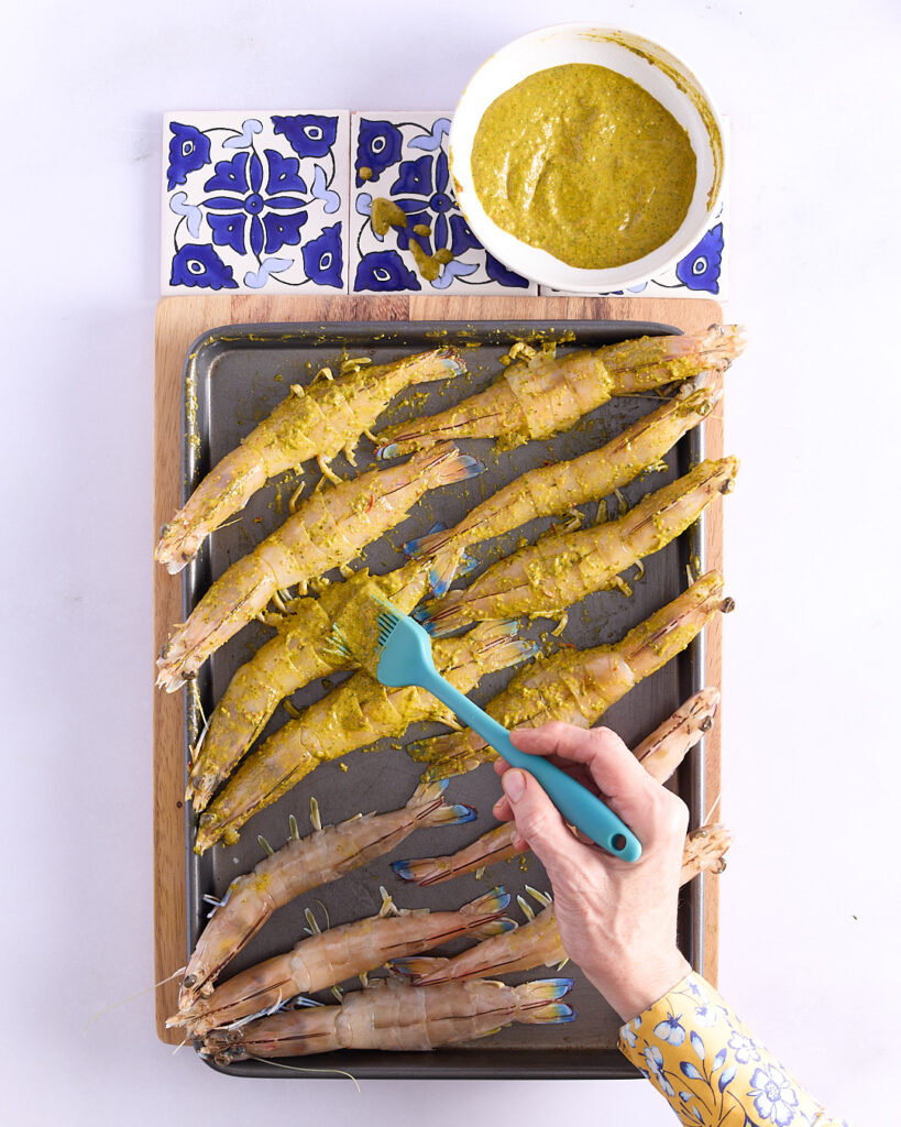 Sandra basting the butterflied prawns on a cooking tray with chermoula.