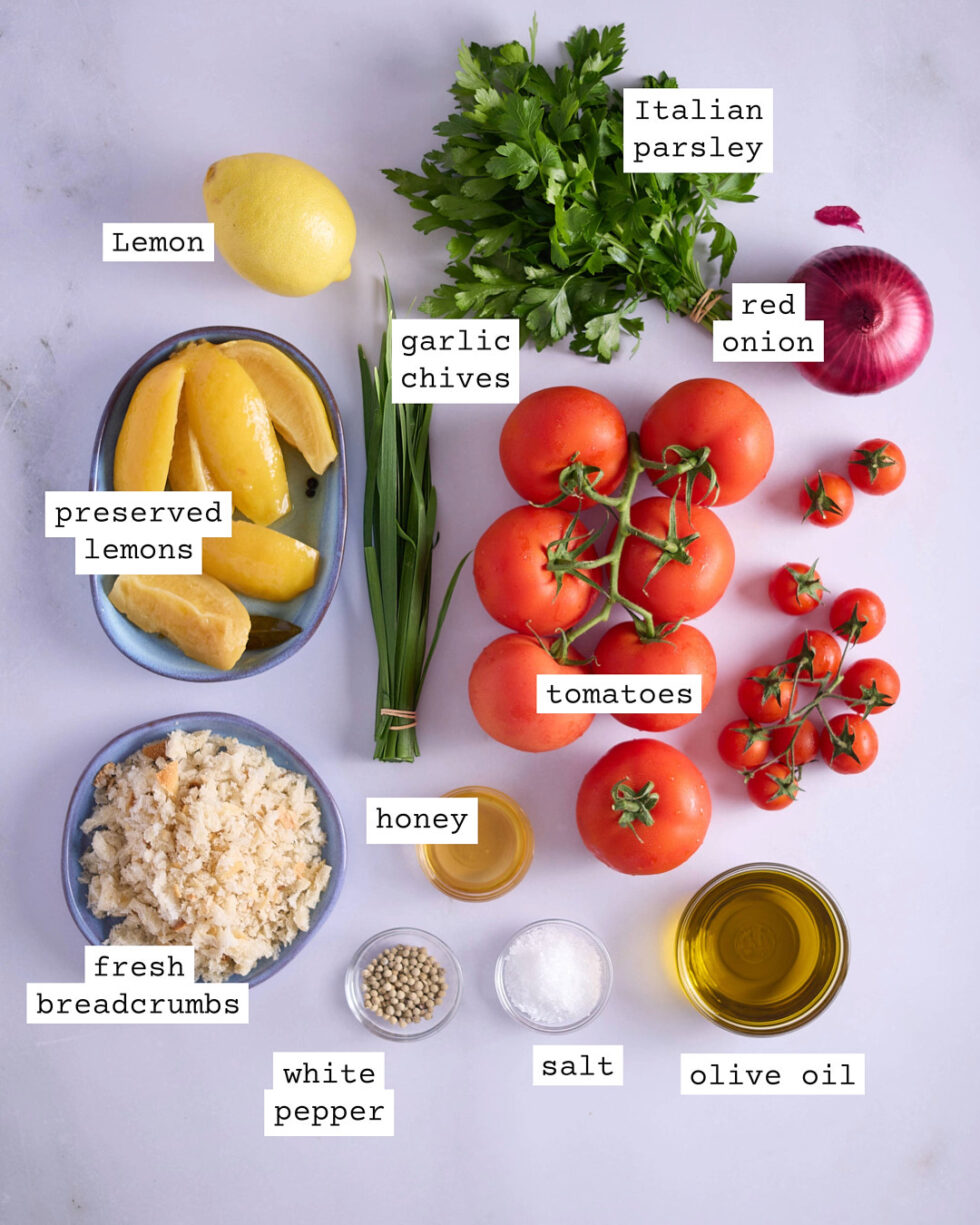 Ingredients for tomato and preserved lemon salad on a white marble bench.