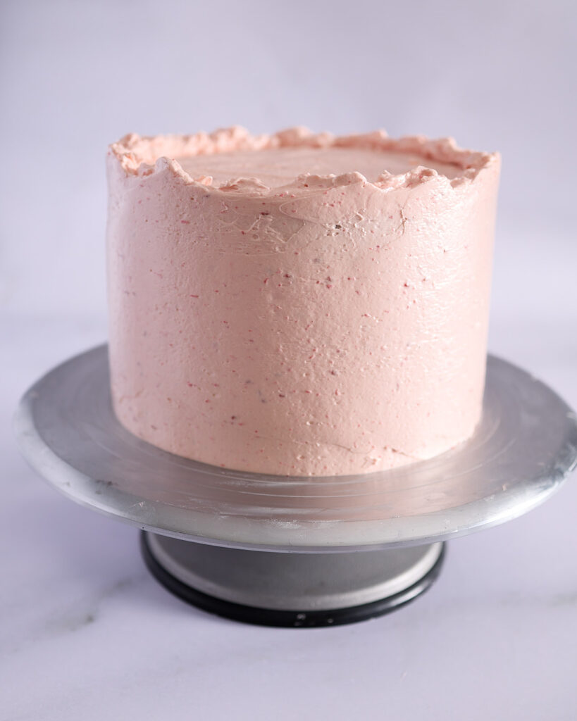 Fully frosted three-layer chocolate cake with a smooth raspberry buttercream finish and a rustic top edge created by gently swirling frosting inward.