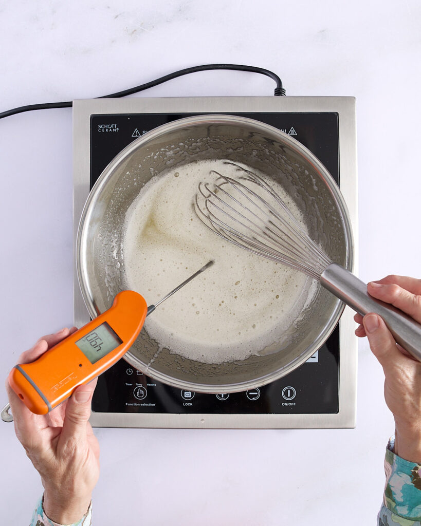 Sandra whisking egg whites and sugar in a metal bowl over a double boiler with a thermometer reading 70°C, step one in making Swiss meringue buttercream.