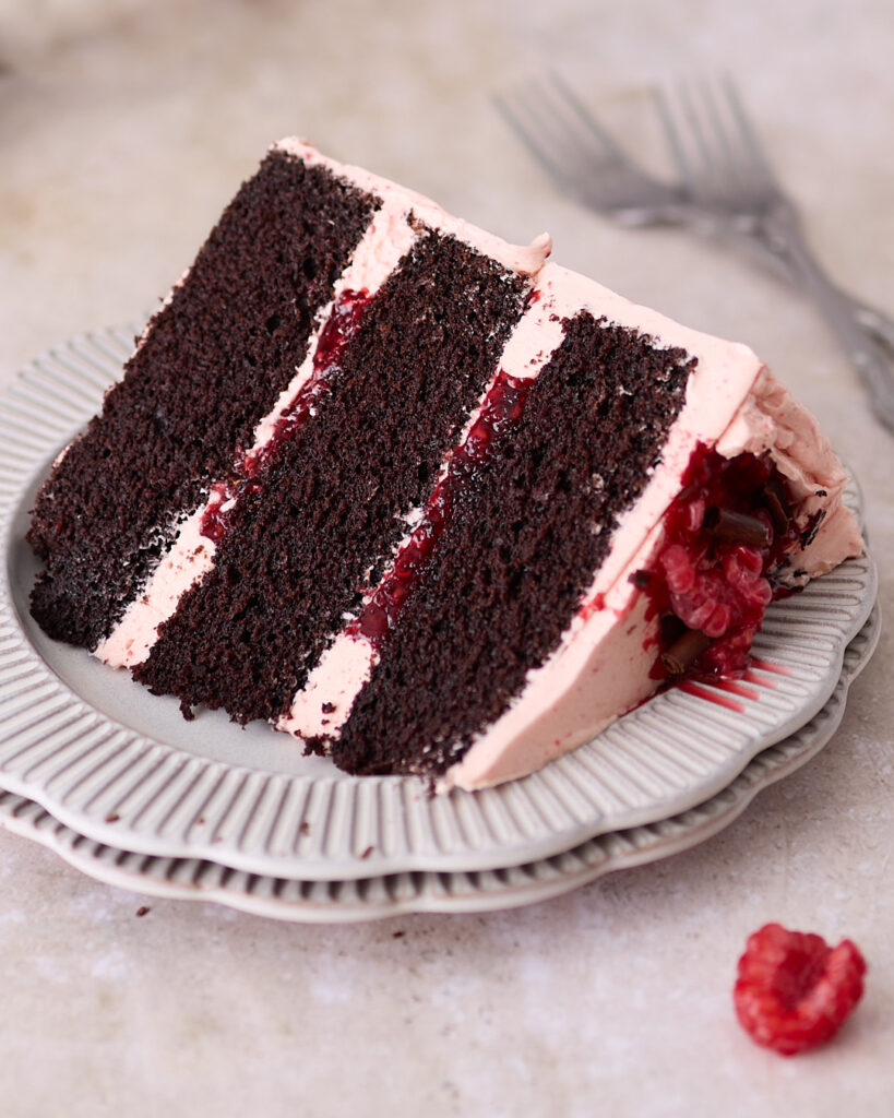 Three-layered Devil's food cake with fresh raspberry Swiss meringue buttercream served on a fluted white plate.