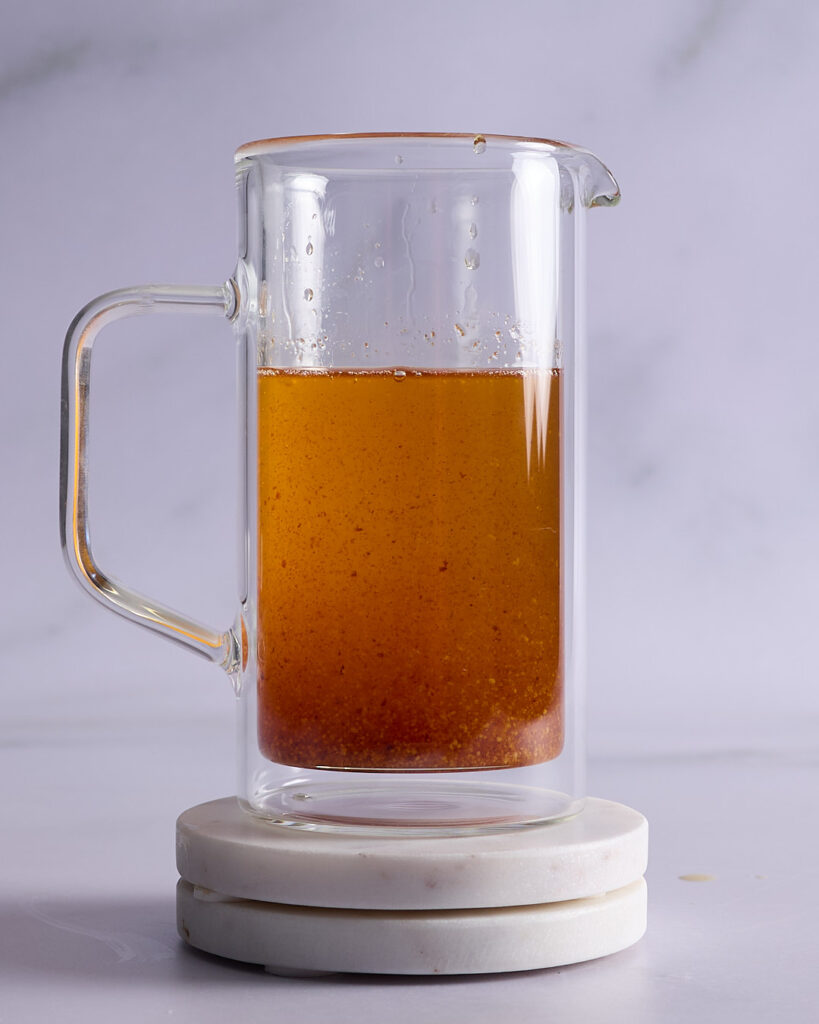 A glass jug of browned butter showing golden liquid and toasted milk solids.
