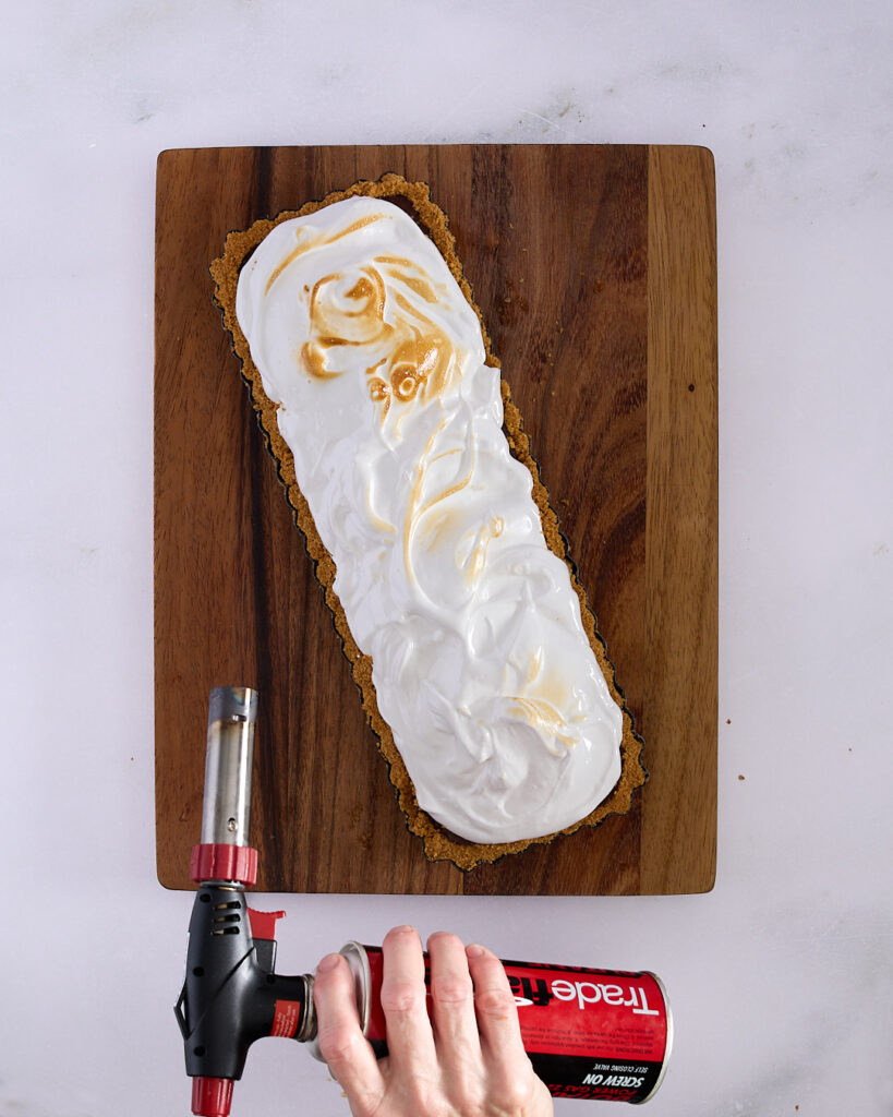 Sandra using a kitchen blowtorch to toast the marshmallow layer on top of a chocolate raspberry marshmallow tart.