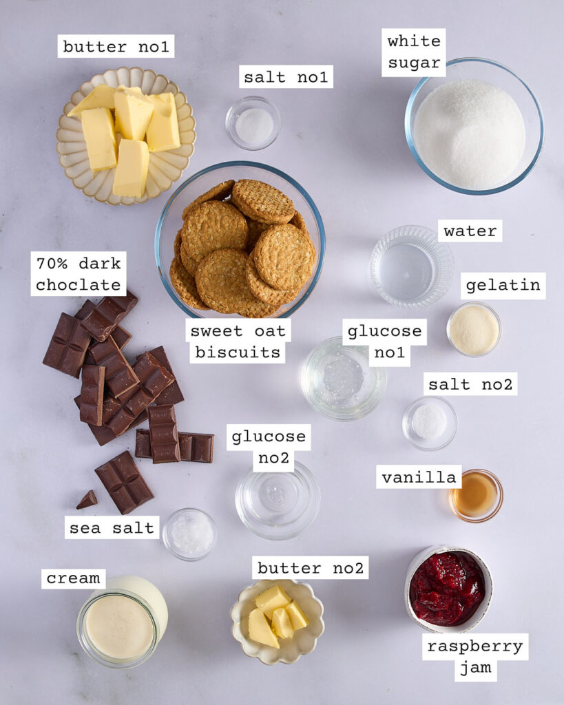 Overhead shot of labelled ingredients for a chocolate raspberry marshmallow tart, including sweet oat biscuits, dark chocolate, raspberry jam, cream, glucose, gelatin, and butter.