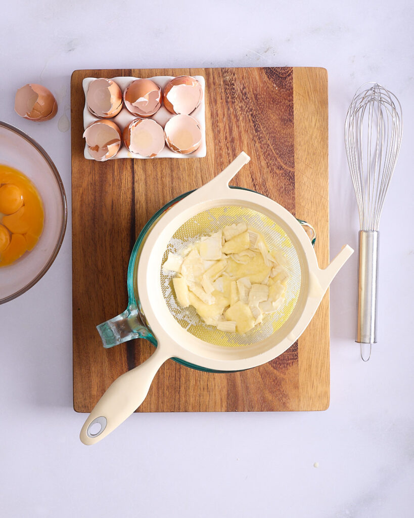 Melted cheese mixture being strained through a sieve.