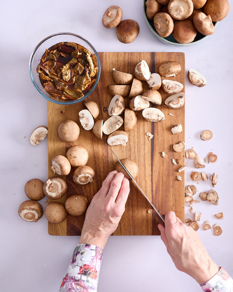 Sandra slicing Swiss brown mushrooms with rehydrating porcini mushrooms in a glass bowl.