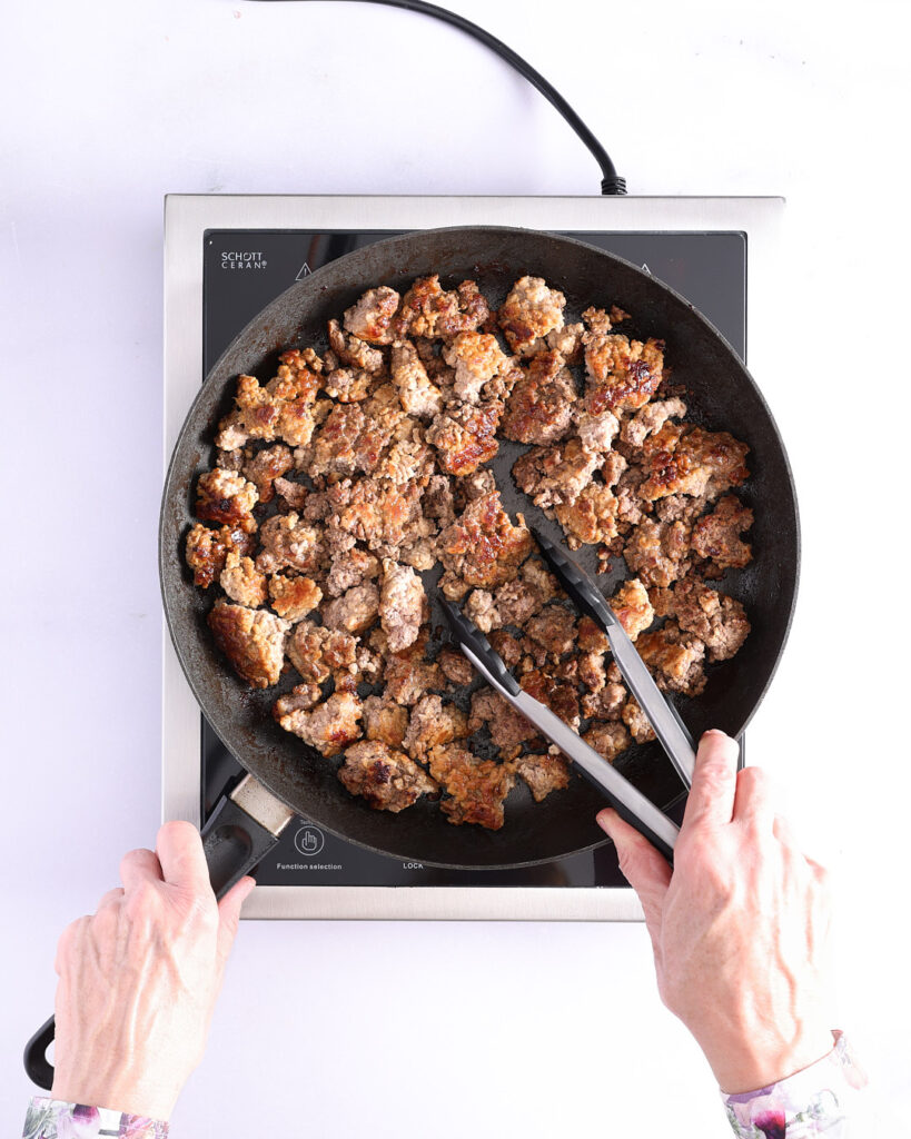 Sandra has partially turned the sizzling ground beef and pork mince, showing the batch cooking process.