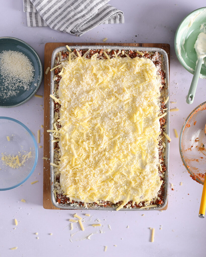 Ready for baking with a thick layer of béchamel sauce, topped with shredded mozzarella, Parmigiano Reggiano, and flecks of stracciatella cheese.