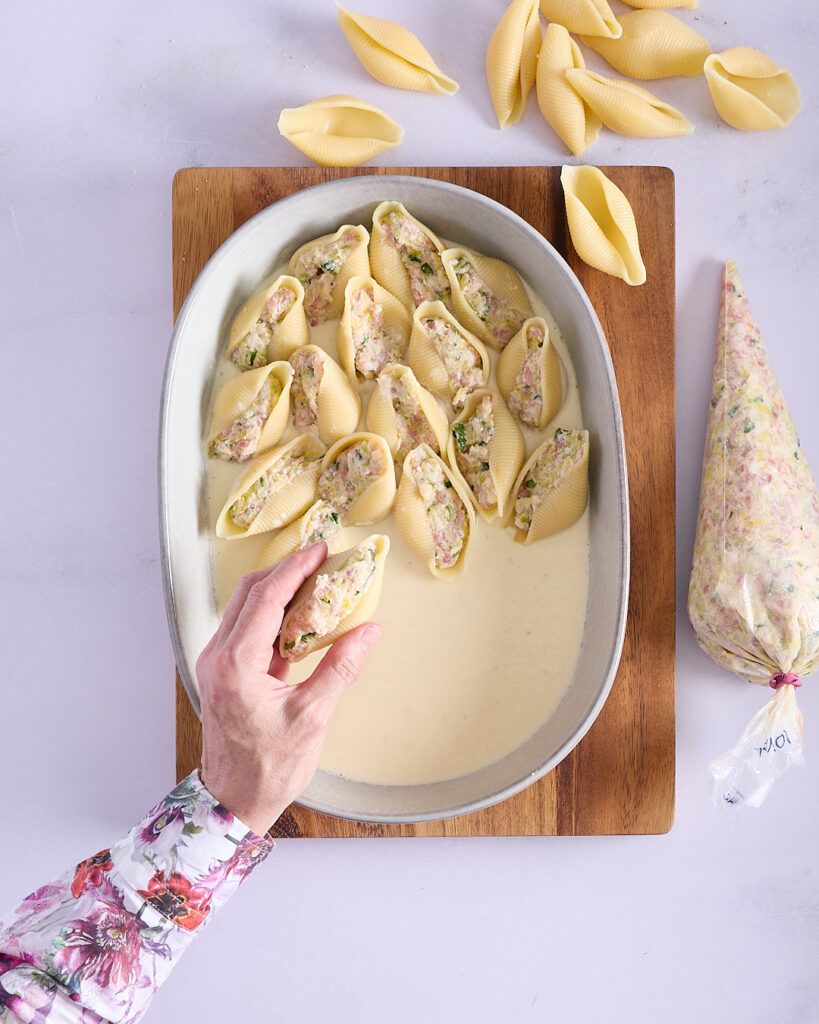 Sandra placing stuffed pasta shells into stoneware dish.