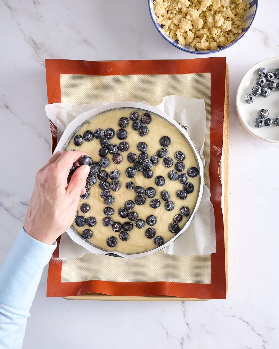 Sandra scattering fresh blueberries over cheesecake batter in a springform pan, the next step in making a blueberry rosemary crumble cheesecake.