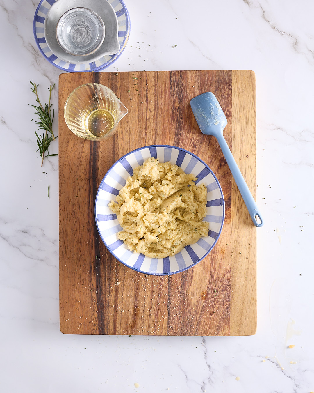 Bowl of freshly mixed rosemary crumble for a low sugar blueberry ricotta cheesecake recipe, showing coarse crumbs and a silicone spatula on a wooden board.