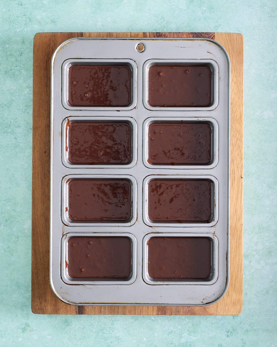 Chocolate cake batter portioned into an eight-hole mini loaf pan, with each cavity filled to about one centimetre below the rim, ready to bake.