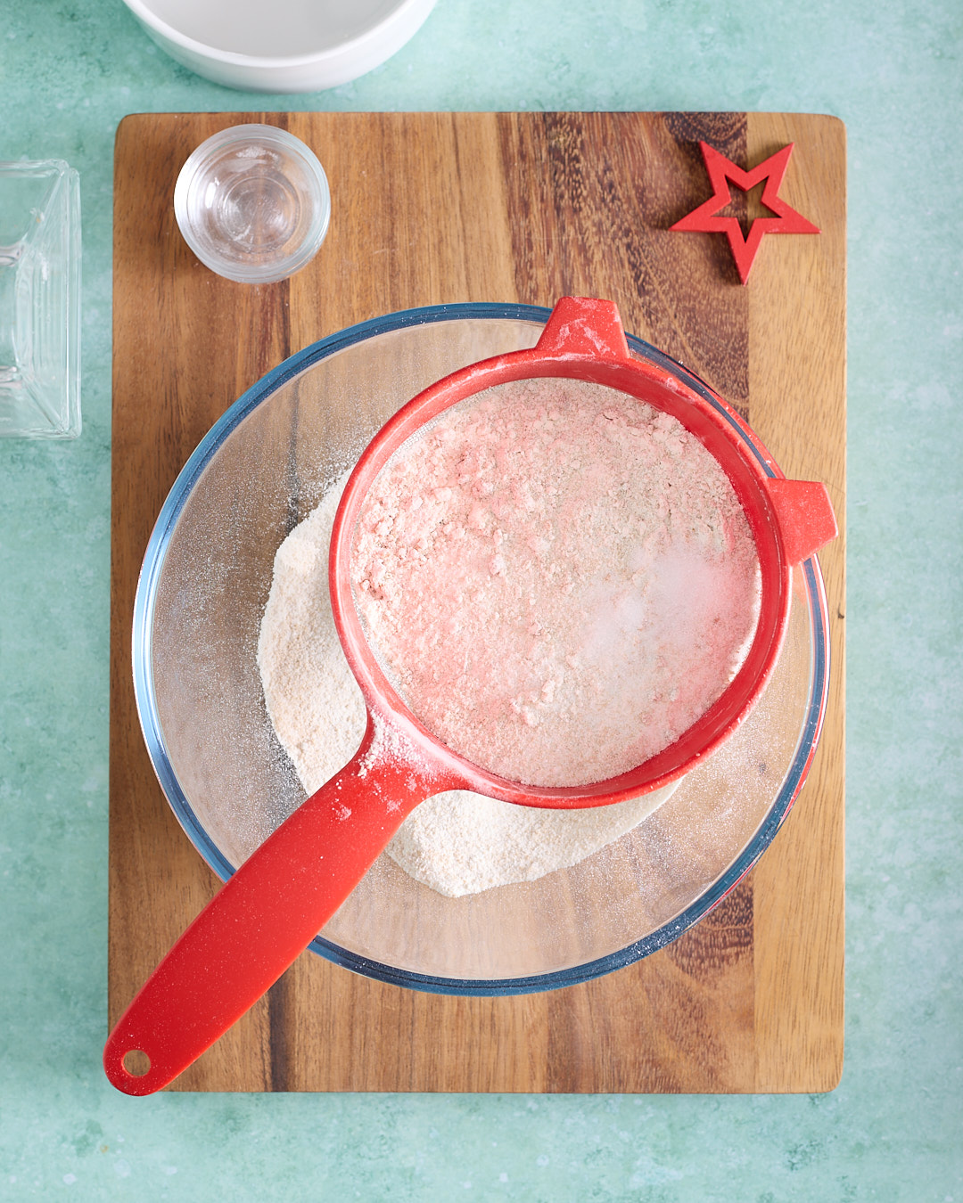Sifting the flour, baking powder, baking soda, salt, white sugar, and brown sugar into a large mixing bowl with a coarse sieve while the cocoa and espresso mixture cools to room temperature, creating a fine, evenly combined dry mix with no lumps.