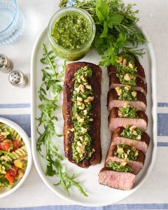 Sliced lamb roast topped with spoonfuls of mixed herb walnut pesto and chopped walnuts.