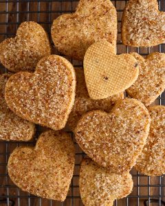 Heart-shaped shortbread biscuits dusted with citrus and pink peppercorn sugar cooling on a wire rack.