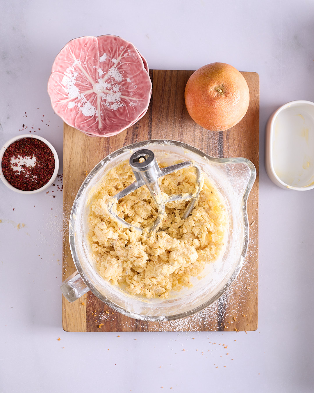 A shaggy, crumbly shortbread dough beginning to come together in a glass mixing bowl.