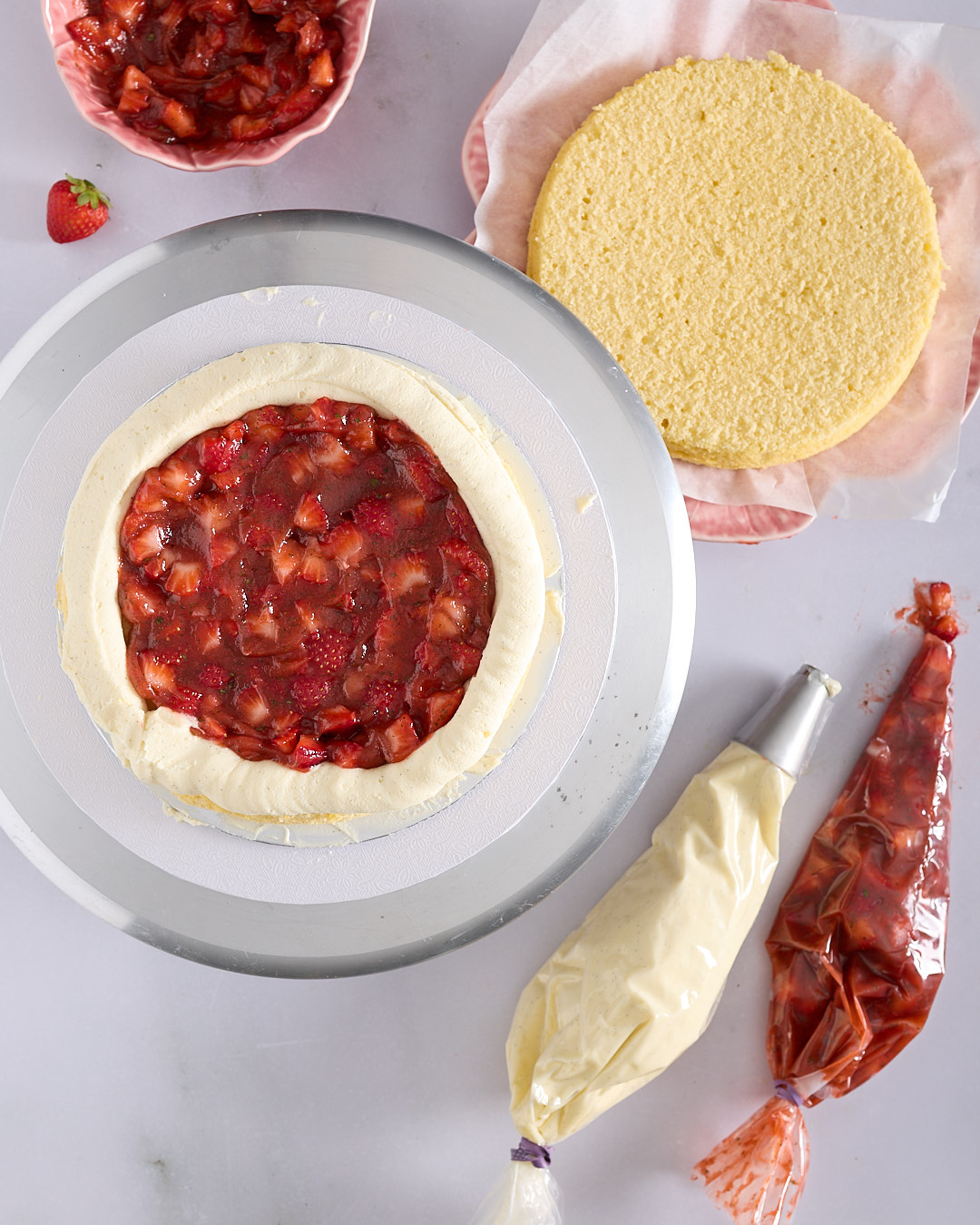 Overhead view of a vanilla chiffon cake layer on a turntable with a piped dam of white chocolate ganache filled with chunky strawberry basil gel.