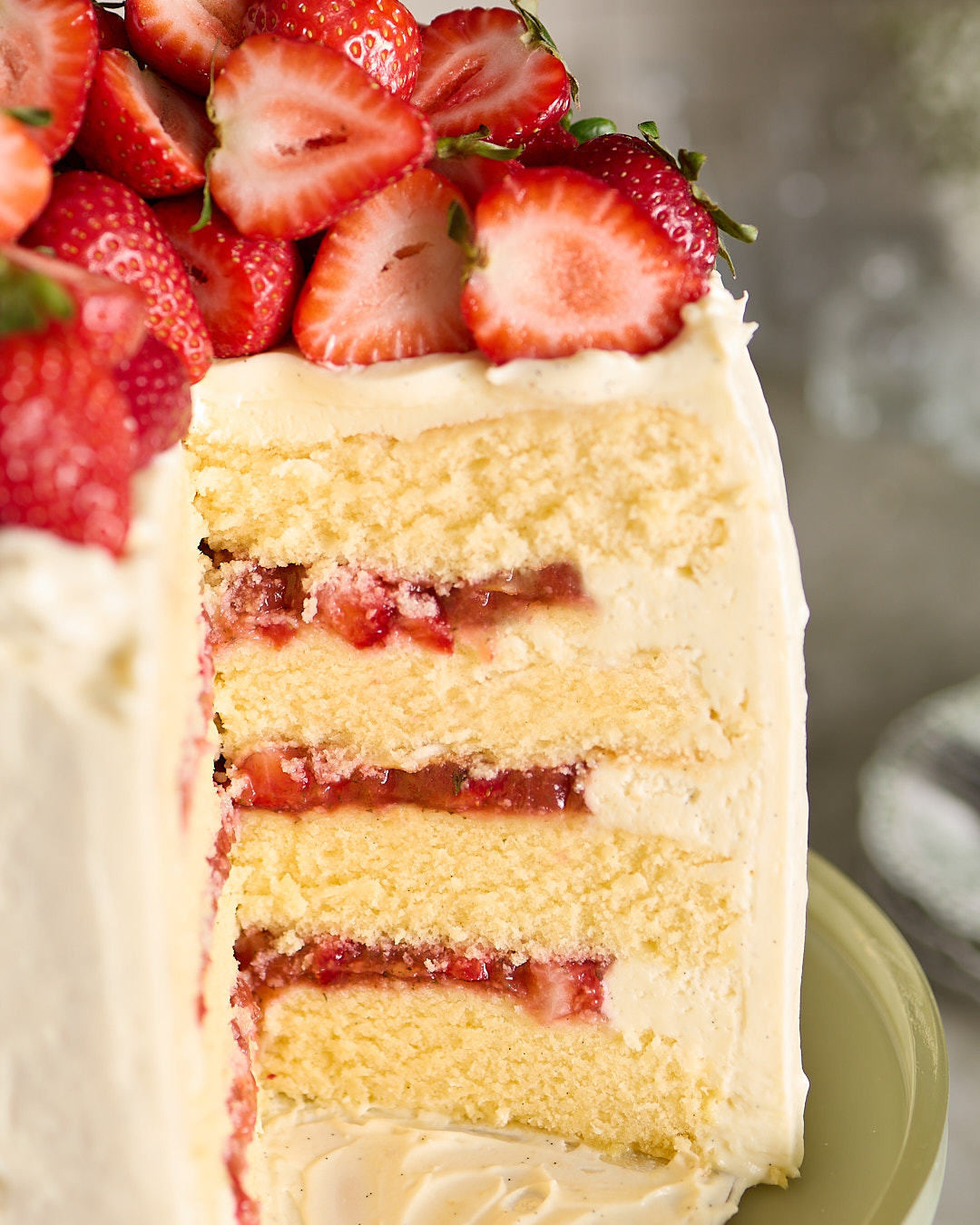 Close-up of a slice of strawberry basil white chocolate chiffon cake showing layers of sponge, whipped ganache, and strawberry basil gel topped with fresh halved strawberries.