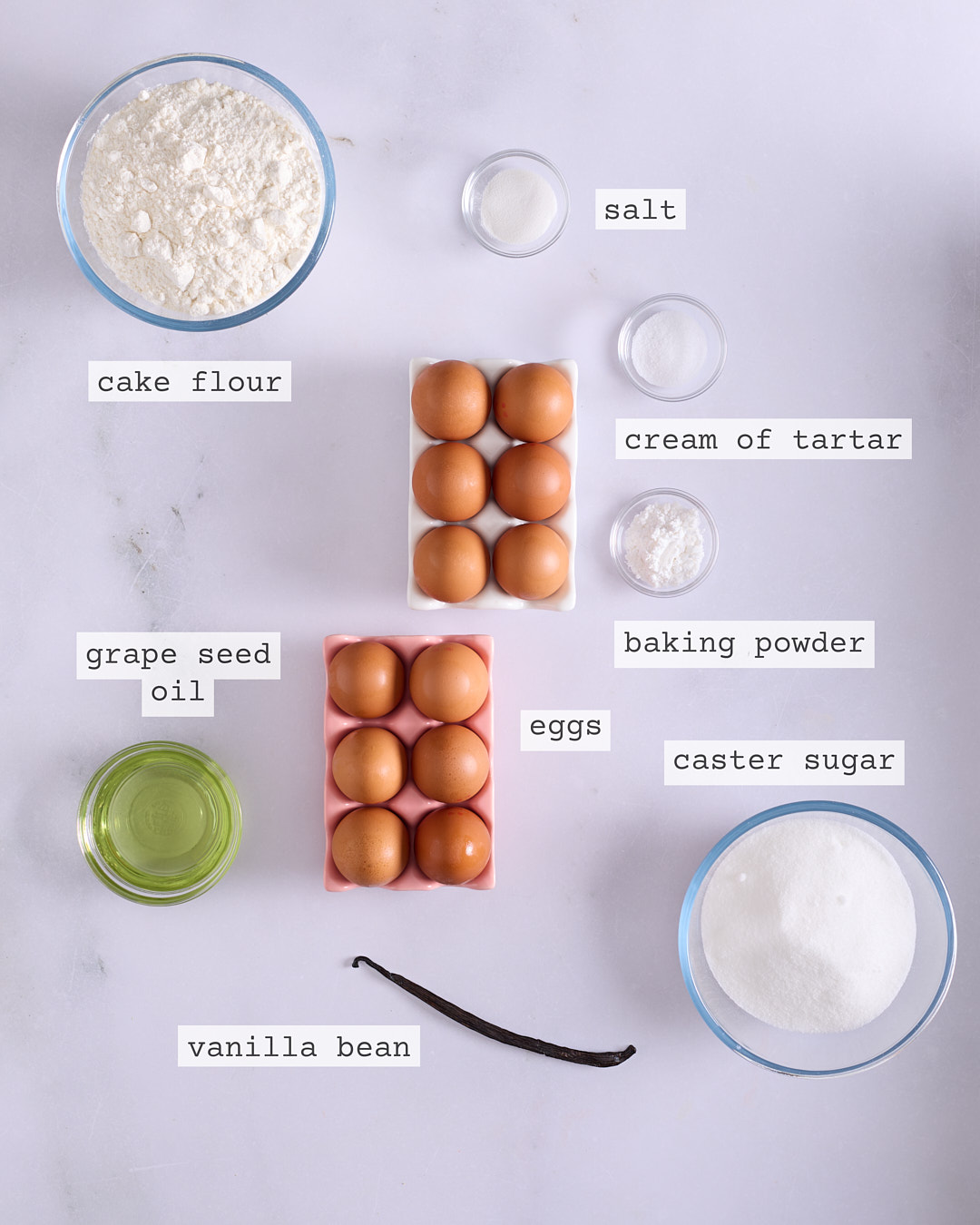 Flat lay of ingredients for vanilla chiffon cake including cake flour, eggs, grapeseed oil, caster sugar, vanilla bean, cream of tartar, baking powder, and salt.
