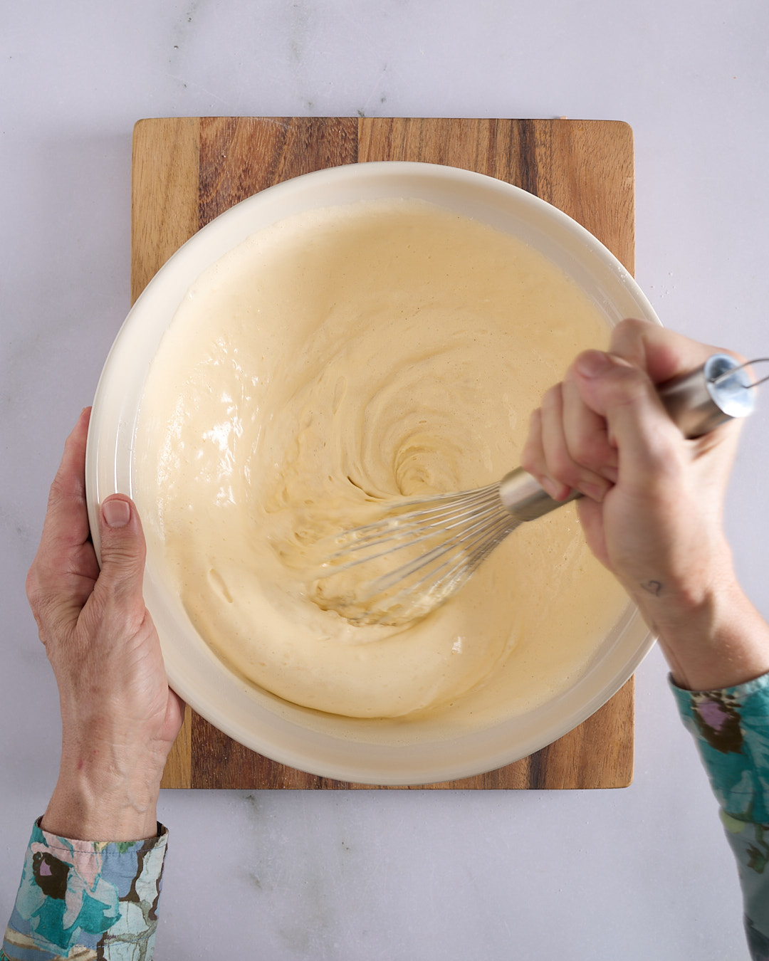 Sandra using a balloon whisk to incorporate a portion of white meringue into a large bowl of pale-yellow aerated egg yolk mixture.