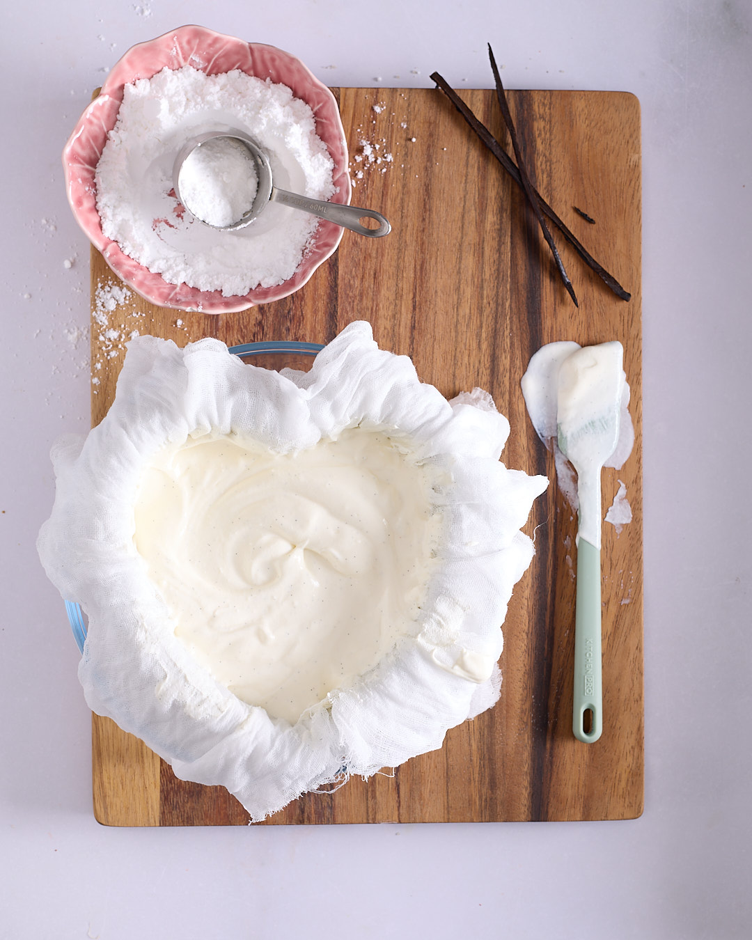 Heart shaped cake pan lined with three layers of damp white cheesecloth and filled with coeur à la crème mixture sitting inside a glass bowl.