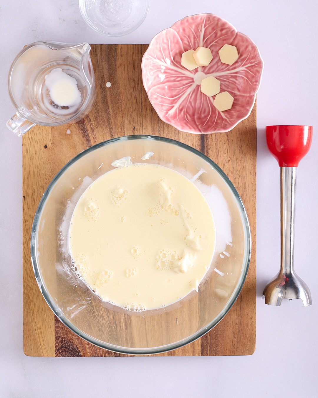 Hot cream poured over softened white chocolate and gelatine in a glass bowl.
