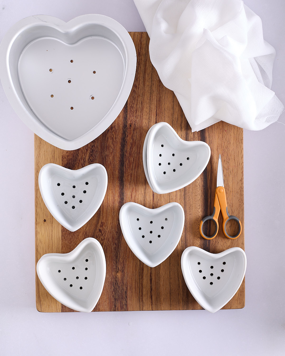 Small porcelain heart shaped moulds with drainage holes and a large heart shaped pan with cheesecloth for a yoghurt coeur à la crème recipe.