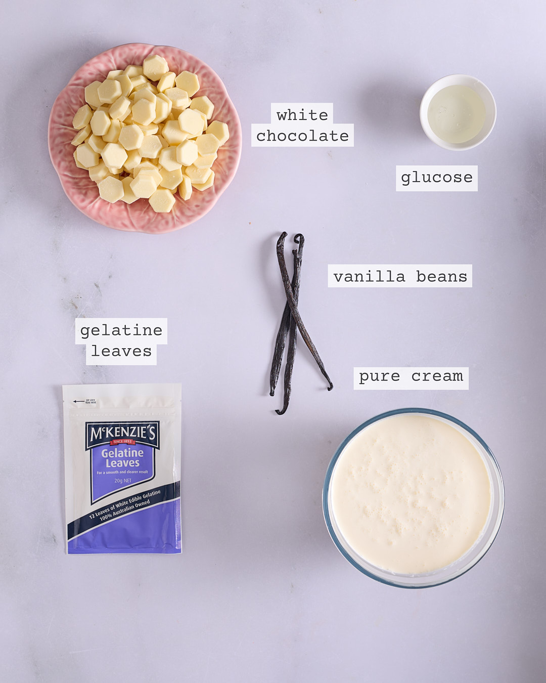 Flat lay of ingredients for whipped white chocolate ganache including white chocolate, glucose, vanilla beans, gelatine leaves and pure cream.