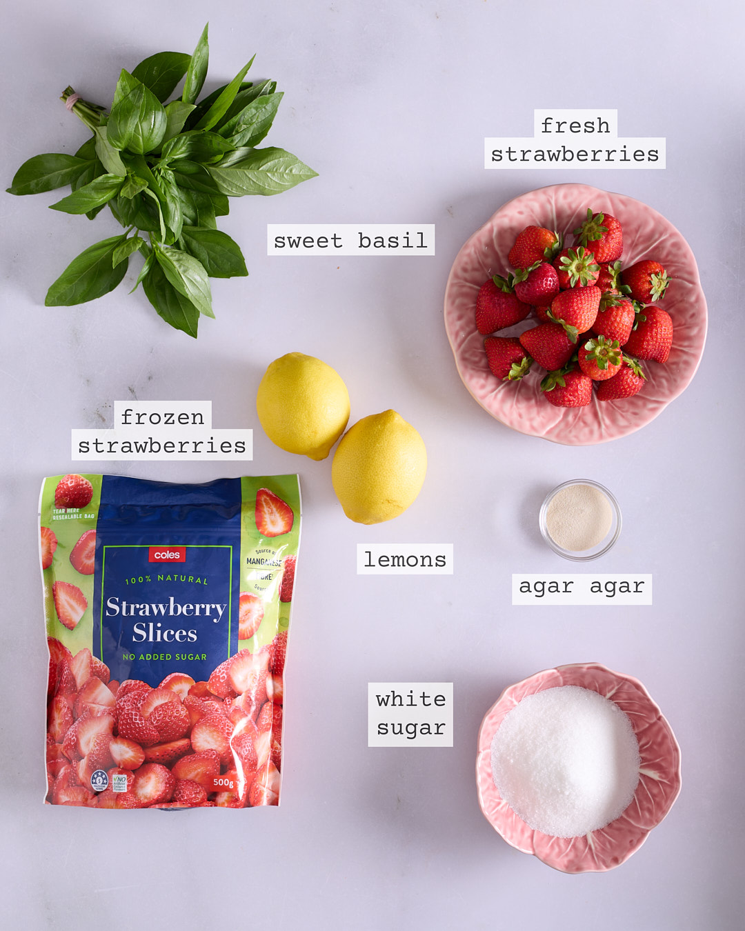 Flat lay of ingredients for strawberry and sweet basil fluid gel including frozen and fresh strawberries, lemons, sugar, basil and agar-agar.