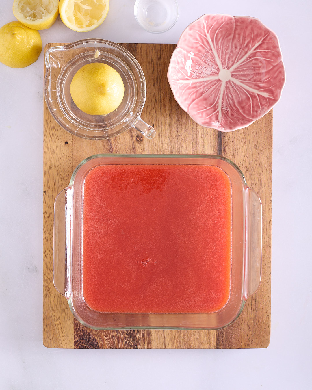 Smooth strawberry mixture setting in a square glass Pyrex dish on a wooden board.