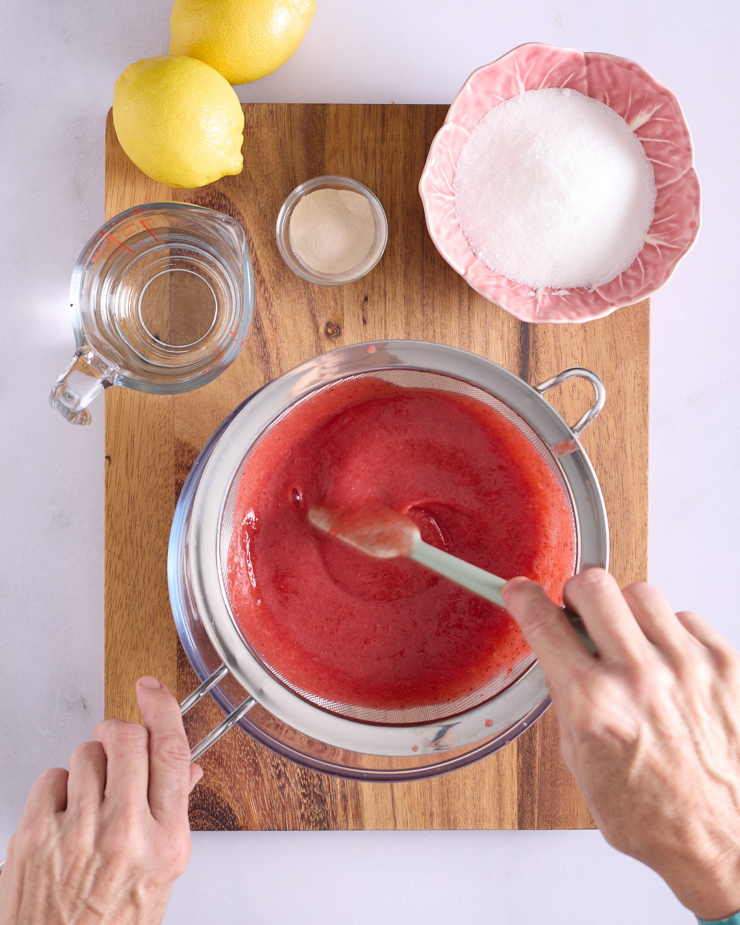 Sandra using a spatula to press strawberry puree through a fine mesh sieve into a bowl.